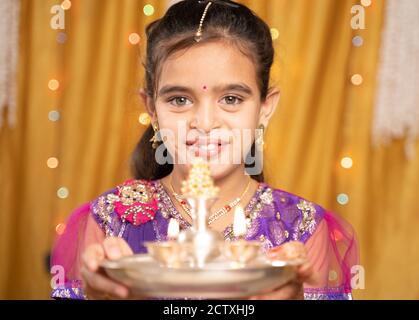 POV shot of cute little girl in traditional dress doing aarti or offering light to god during Hindu Religious festival ceremony. Stock Photo