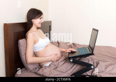Pregnant Woman Using Laptop Computer in home on bed. Pregnant morning work concept. Stock Photo