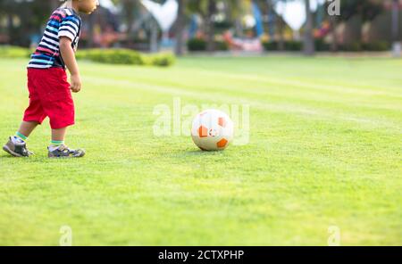 Young little boy learning to play soccer getting ready to kick the ball on the grass at a park on a summer day. Stock Photo