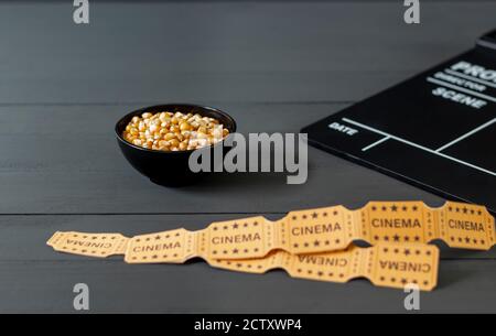 Bowl with corn kernels, to prepare popcorns, next to a clapperboard on a black wooden background. Film and television industry, selective focus, conce Stock Photo