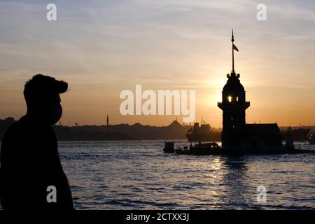 Silhouette of a young man who is wearing a face mask protecting against corona virus and silhouette of The Maidens Tower at Istanbul Stock Photo