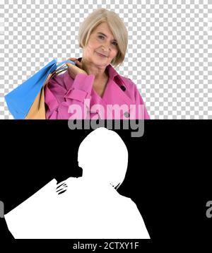Beautiful senior woman in trench coat holding shopping bags, Alp Stock Photo
