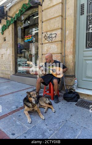 Young man man plays an ancient stringed instrument on the street for Heraklion Greece. His dog is sitting next to him Stock Photo