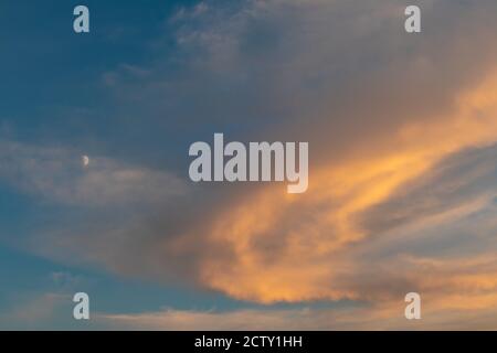 Sunset colorful epic colorful golden clouds on blue vivid sky with early moon. Magic dusk light cloudscape Stock Photo