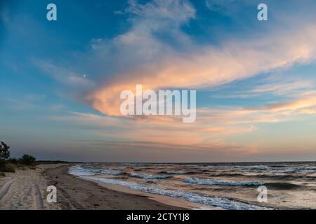 Sunset epic colorful clouds on blue sky with stormy white waves on sea shore sand beach. Magic evening landscape Stock Photo