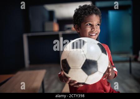 A little soccer player posing with the ball in a locker room Stock Photo