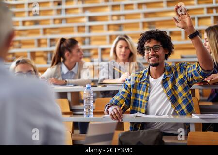 Male student raising the hand for a question at the lecture in the university classroom Stock Photo
