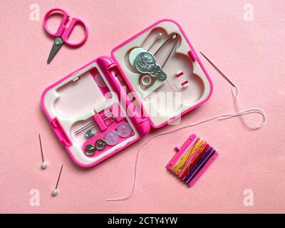 Close up of little pink opened sewing kit with scissors, needle with thread and pins around Stock Photo