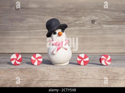 Playful Christmas concept. Miniature snowman with candies in front of soft wood background. Handmade with clay. Stock Photo