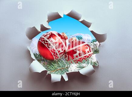 vRed Christmas trinkets on fir twigs visible through hole torn in craft paper. Creative concept of sudden Xmas season. Stock Photo
