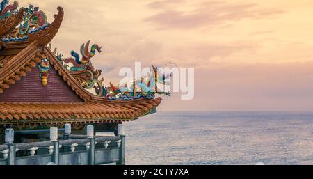 A large beautiful temple overlooking coast in Taiwan island. Beauty chinese dragon statue made by a pieces of colorful ceramic on the roof with sunset Stock Photo