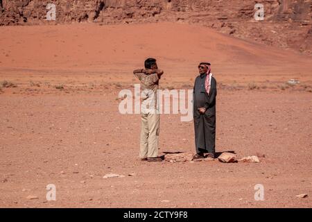 Wadi Rum, Jordan 04/01/2010: Two men are seen having a conversation in the middle of desert. One stretches arms and the other one wearing a thobe, kef Stock Photo