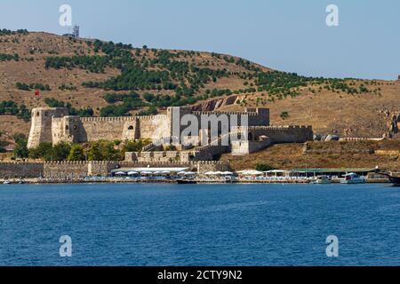 Landscape view of the coast of Bozcaada (Tenedos), Turkey. Image features a medieval castle, tourist shops, beach umbrellas and some boats along the s Stock Photo