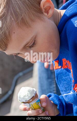 Barcelona, Spain 05/01/2010: A blond eight year old boy wearing a blue hoodie is holding a cone of vanilla ice cream in his hands. His mouth is smeare Stock Photo