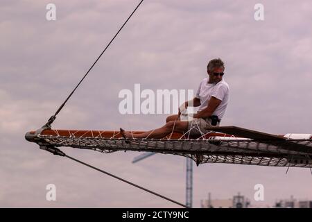 Barcelona, Spain, 05/01/2010: An athletic sailor is sitting on top of the wooden bowsprit of a large vessel trying to fix it. He wears no protective e Stock Photo