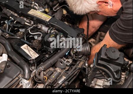 Senior Mechanic working on engine bay repairing a oil leak in home garage Stock Photo