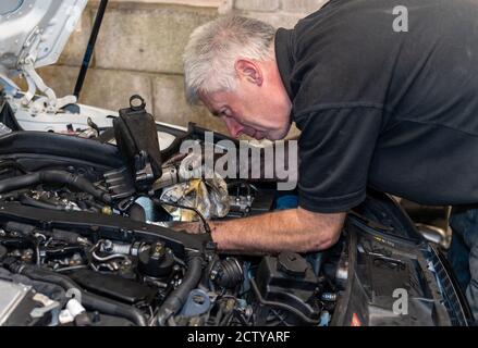 Senior Mechanic working on engine bay repairing a oil leak in home garage Stock Photo