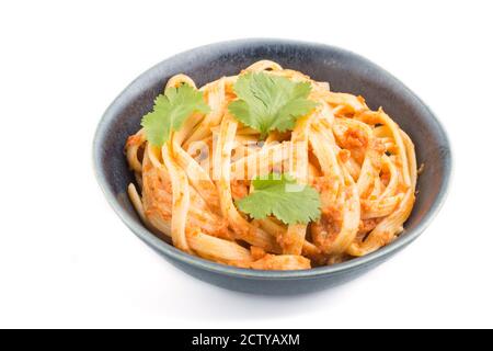 Semolina pasta with tomato pesto sauce, orange and herbs in bowl isolated on white background. Side view, close up. Stock Photo