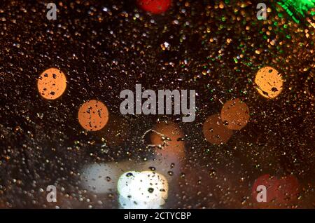 Raindrops on the glass of the car lit by street lamps in the night. Stock Photo