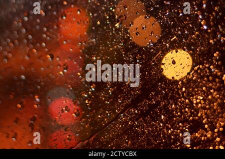 Raindrops on the glass of the car lit by street lamps in the night. Stock Photo