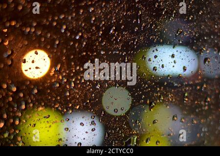 Raindrops on the glass of the car lit by street lamps in the night. Stock Photo