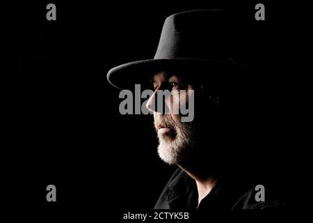 Close-up portrait of bearded middle-aged man in wide-brimmed western hat against a dark background Stock Photo