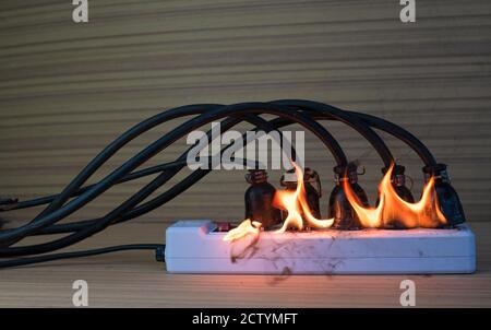 On fire multi socket with the connected power strip with a bunch of plugs on wood background Stock Photo