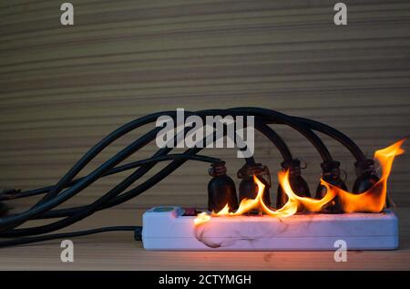 On fire multi socket with the connected power strip with a bunch of plugs on wood background Stock Photo