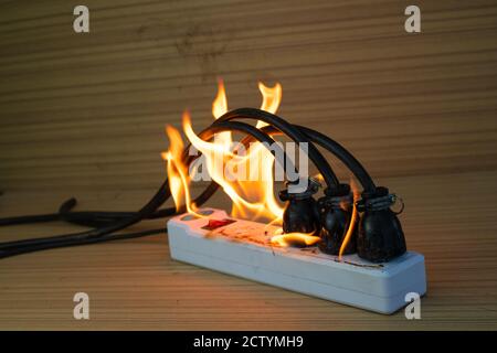 On fire multi socket with the connected power strip with a bunch of plugs on wood background Stock Photo