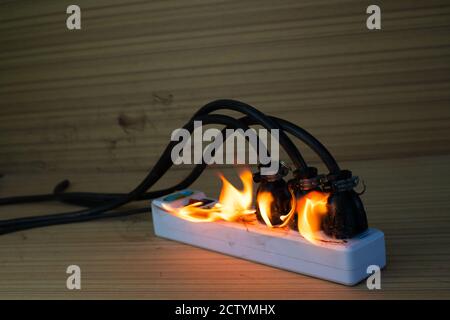 On fire multi socket with the connected power strip with a bunch of plugs on wood background Stock Photo