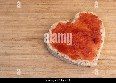 Slice of bread in heart shape. Healthy whole wheat bread with strawberry jam on wood cutting board. Concept about love, Valentines day. Copy space. Stock Photo
