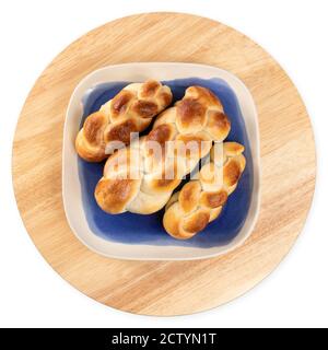 Multiple small braided buns on a blue plate and round wood board. Baked yeast bread with egg wash, Top view. Authentic Swiss butter bread recipe calle Stock Photo