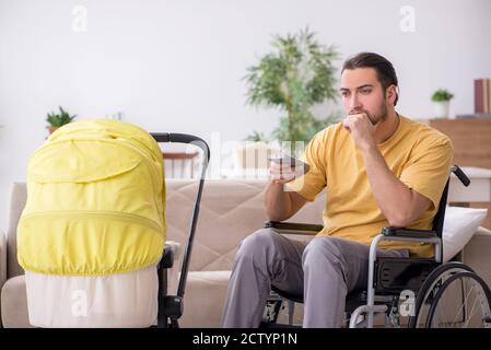 Young man in wheel-chair looking after newborn Stock Photo