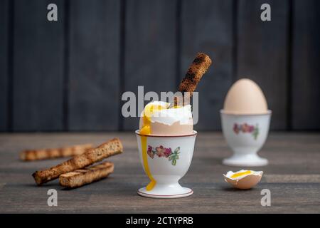 Soft boiled brown egg and toast bread in eggcup on wooden table background. Close up. Healthy breakfast Stock Photo