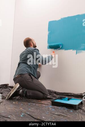 Father preparing the baby's room using blue color. Home during renovation, decoration and painting. Interior apartment improvement maintenance. Roller, ladder for house repair Stock Photo