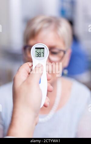 Senior patient having high temperature measured using infrared thermometer during medical examination. Consultation for infections and disease during global pandemic, flu, tool, sickness. Stock Photo