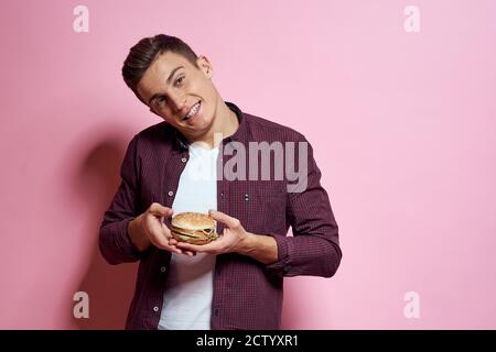 hungry man with hamburgers in hands fast food diet food emotions pink background Stock Photo