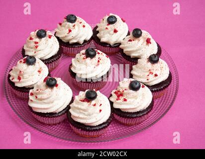 Purple muffins with white whipped cream and a blueberry on top. Round plate on a purple background. Space for text. Stock Photo