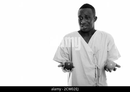 Studio shot of young black African man patient looking confused with two apples Stock Photo