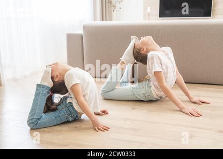 Two girls sisters practicing yoga at home, stretching in King Cobra pose Stock Photo