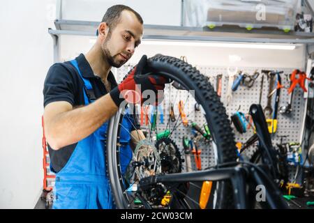 Bicycle assembly in workshop, man installs wheel Stock Photo