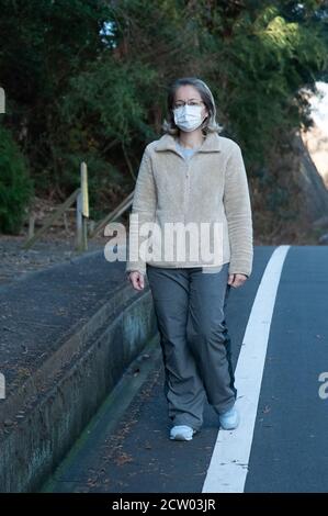 Woman 40-49 year old outdoors wearing glasses and white mask for protection against Coronavirus (COVID-19) and other contagious diseases. Stock Photo