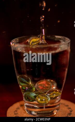 splash of drops in a glass of water and marbles or colors glass balls Stock Photo