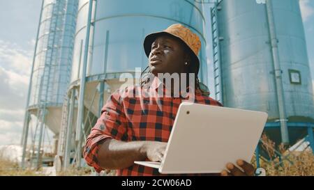 African farmer using laptop in front of the silo storage system. High quality photo Stock Photo