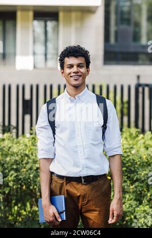Handsome young man going standing outdoors with backpack and notebook Stock Photo