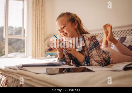 Smiling girl lying on bed with books. Girl studying while lying on bed at home. Stock Photo