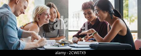 Happy young university students studying with books in library. Group of multiracial people in college library. Stock Photo