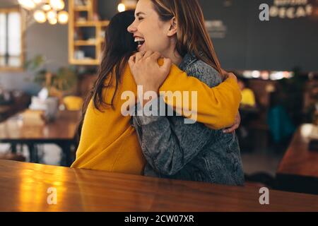 Two young women meeting at a coffee shop. Friends hugging each other at a cafe.