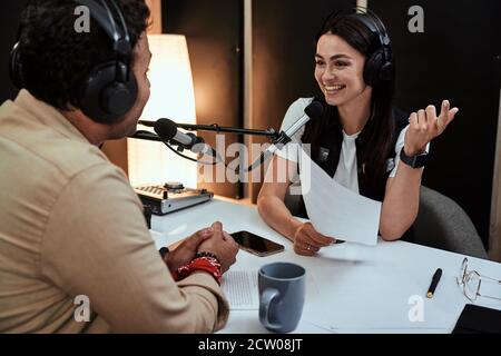 Portait of happy female radio host smiling, talking to male guest, presenter while moderating a live show in studio Stock Photo