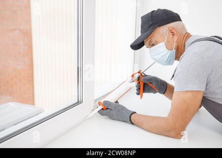 Worker in medical mask use silicone tube gun for repairing and installing window Stock Photo